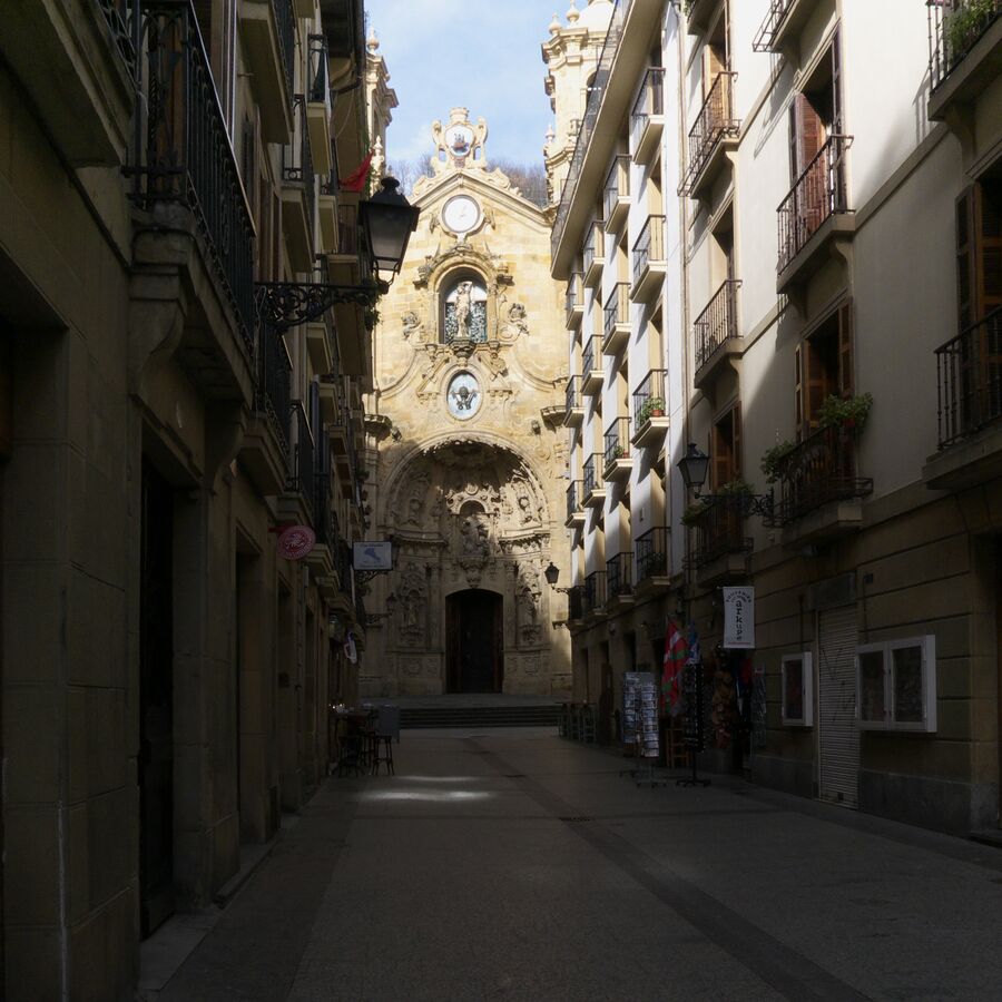 Fachada barroca de la basílica de Santa María del Coro de San Sebastián al fondo de una calle estrecha