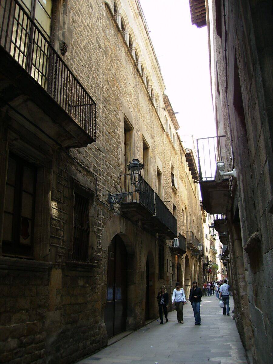 Fachadas de piedra con balcones y portales de arco en el carrer de Montcada, con gente paseando